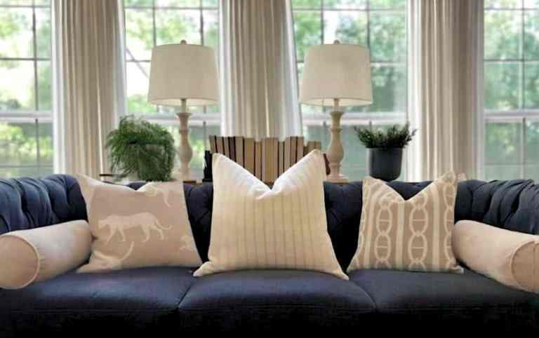 Neutral living room sofa styled with layered throw pillows, lamps, and natural light for a balanced, finished look