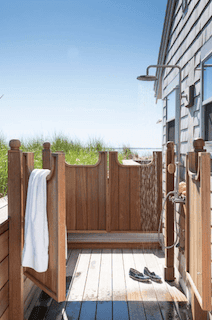Coastal outdoor shower built into a wood deck with privacy walls, rainfall showerhead and ocean view