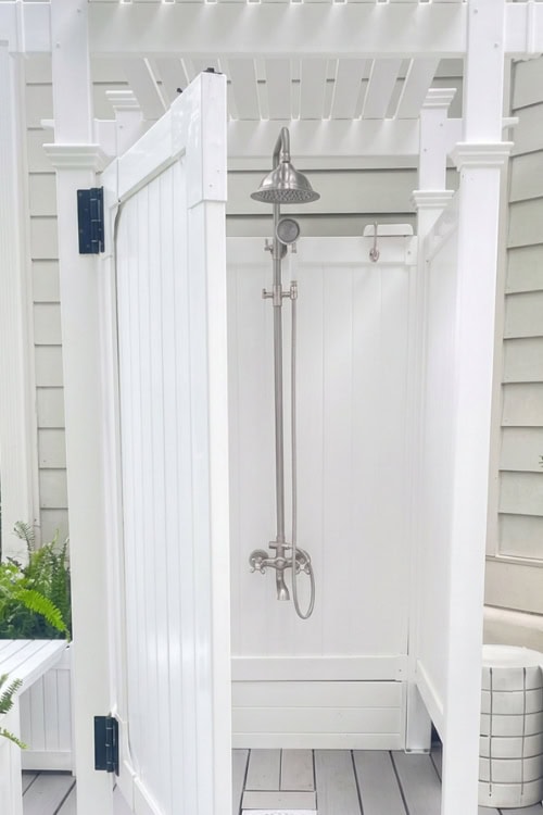 Outdoor white shower stall with silver showerhead and door open