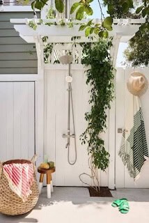 White outdoor shower with pergola-style top, climbing vines, shower fixture and outdoor hooks